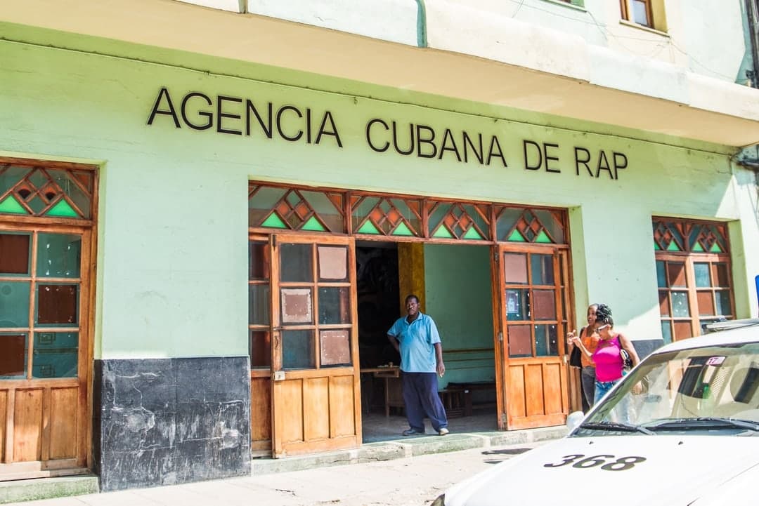 A car is parked in front of a building that says “AGENCIA CUBANA DE RAP”.